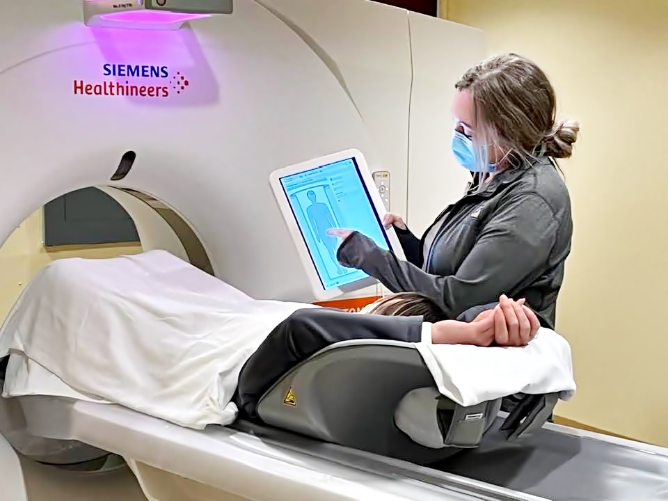 woman receiving information on tablet from a medical advisor as she lays prepared for a cat scan